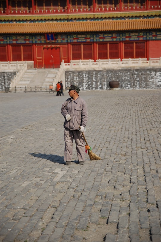 man in gray coat holding brown stick walking on gray concrete pavement during daytime in The Palace Museum China