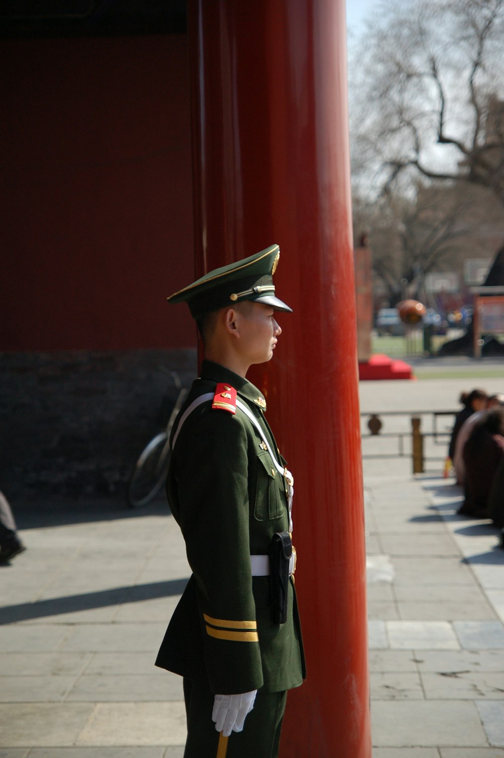 man in green and black camouflage uniform standing near red wall during daytime