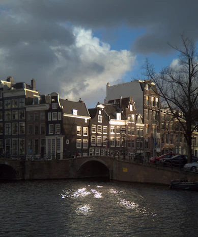 A sleek taxi parked by an Amsterdam canal with historic buildings in the background at sunset.