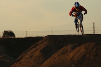 A dynamic shot of Alexandre coaching a BMX rider on a dirt track under a clear sky.