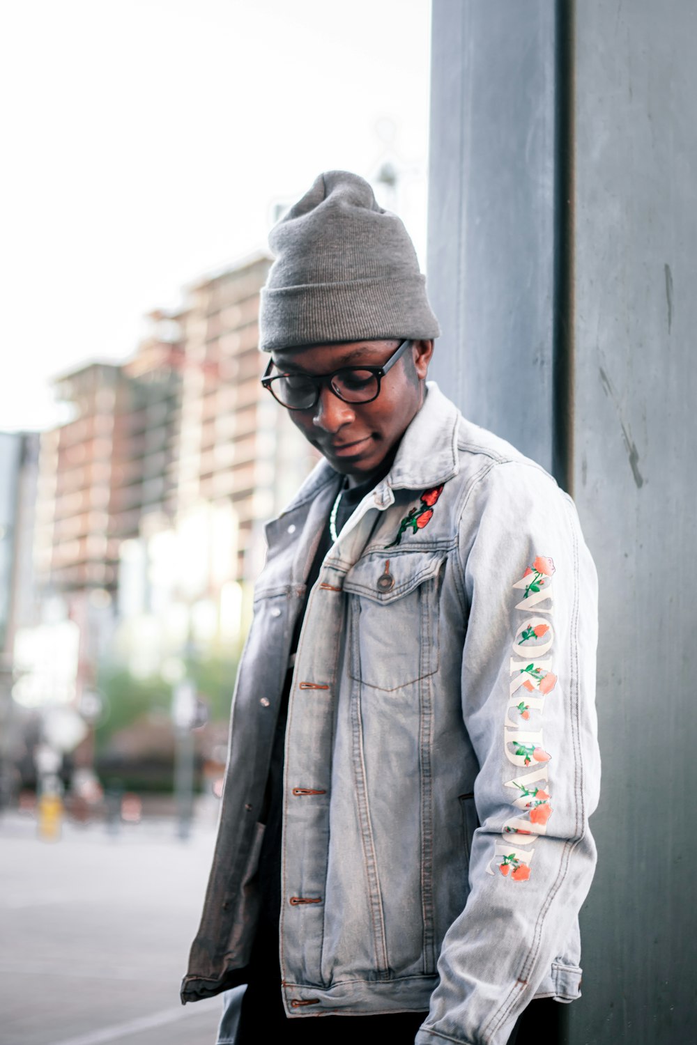 man in blue denim jacket standing near white wall during daytime