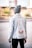 A person is standing with their back to the camera, wearing a stylish denim jacket featuring embroidery and text on the back. The jacket includes floral designs and characters that might be Asian script, and the word 'CULTURE' is prominently displayed. The person is also wearing a gray beanie and dark pants, standing in an urban setting with blurred background elements including trees and buildings.