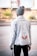 A person is standing with their back to the camera, wearing a stylish denim jacket featuring embroidery and text on the back. The jacket includes floral designs and characters that might be Asian script, and the word 'CULTURE' is prominently displayed. The person is also wearing a gray beanie and dark pants, standing in an urban setting with blurred background elements including trees and buildings.