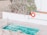 A small swimming pool with clear blue water is surrounded by a tiled patio. There is a pool ladder on one side and a vivid orange life ring hanging on the wall nearby, next to a sign indicating the shallow end as 3ft or 0.9m deep. Tall, spiky plants frame the area, adding a touch of greenery.