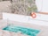 A small swimming pool with clear blue water is surrounded by a tiled patio. There is a pool ladder on one side and a vivid orange life ring hanging on the wall nearby, next to a sign indicating the shallow end as 3ft or 0.9m deep. Tall, spiky plants frame the area, adding a touch of greenery.