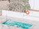 A small swimming pool with clear blue water is surrounded by a tiled patio. There is a pool ladder on one side and a vivid orange life ring hanging on the wall nearby, next to a sign indicating the shallow end as 3ft or 0.9m deep. Tall, spiky plants frame the area, adding a touch of greenery.