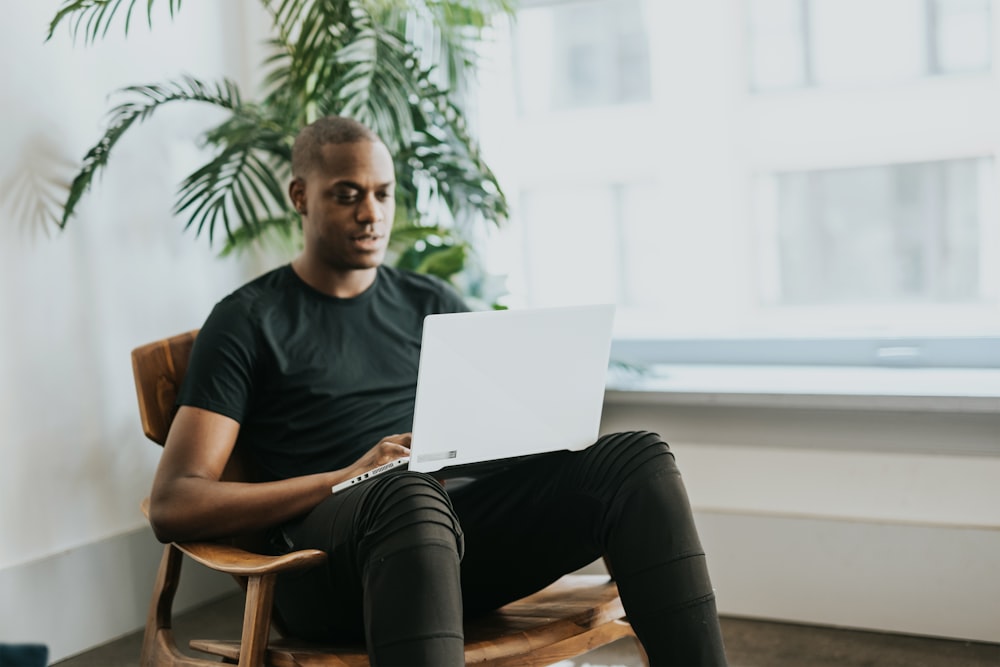 man in black crew neck t-shirt sitting on brown wooden chair using laptop