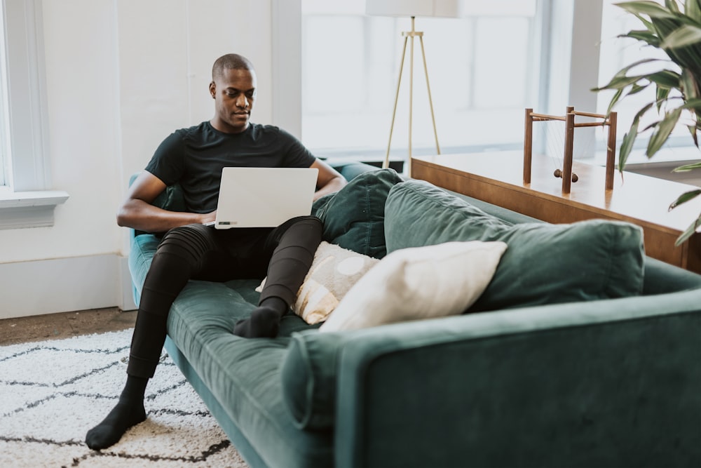 man in black crew neck t-shirt and blue denim jeans sitting on gray couch