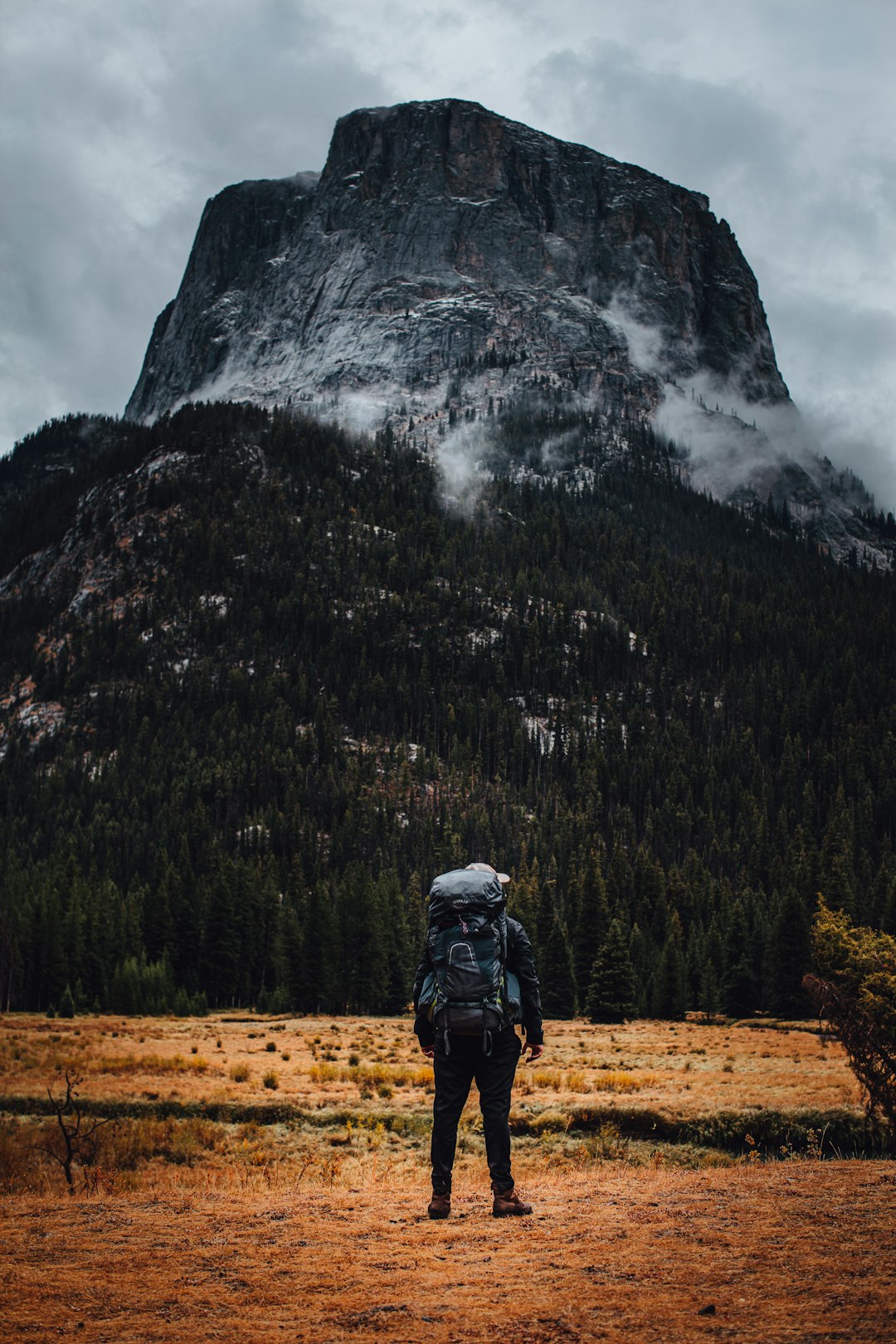 man in black jacket and black pants standing on brown field near mountain during daytime