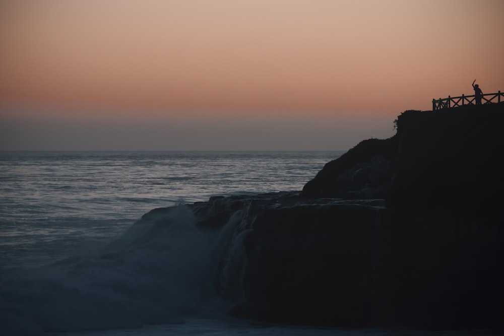 silhouette of rock formation near body of water during sunset