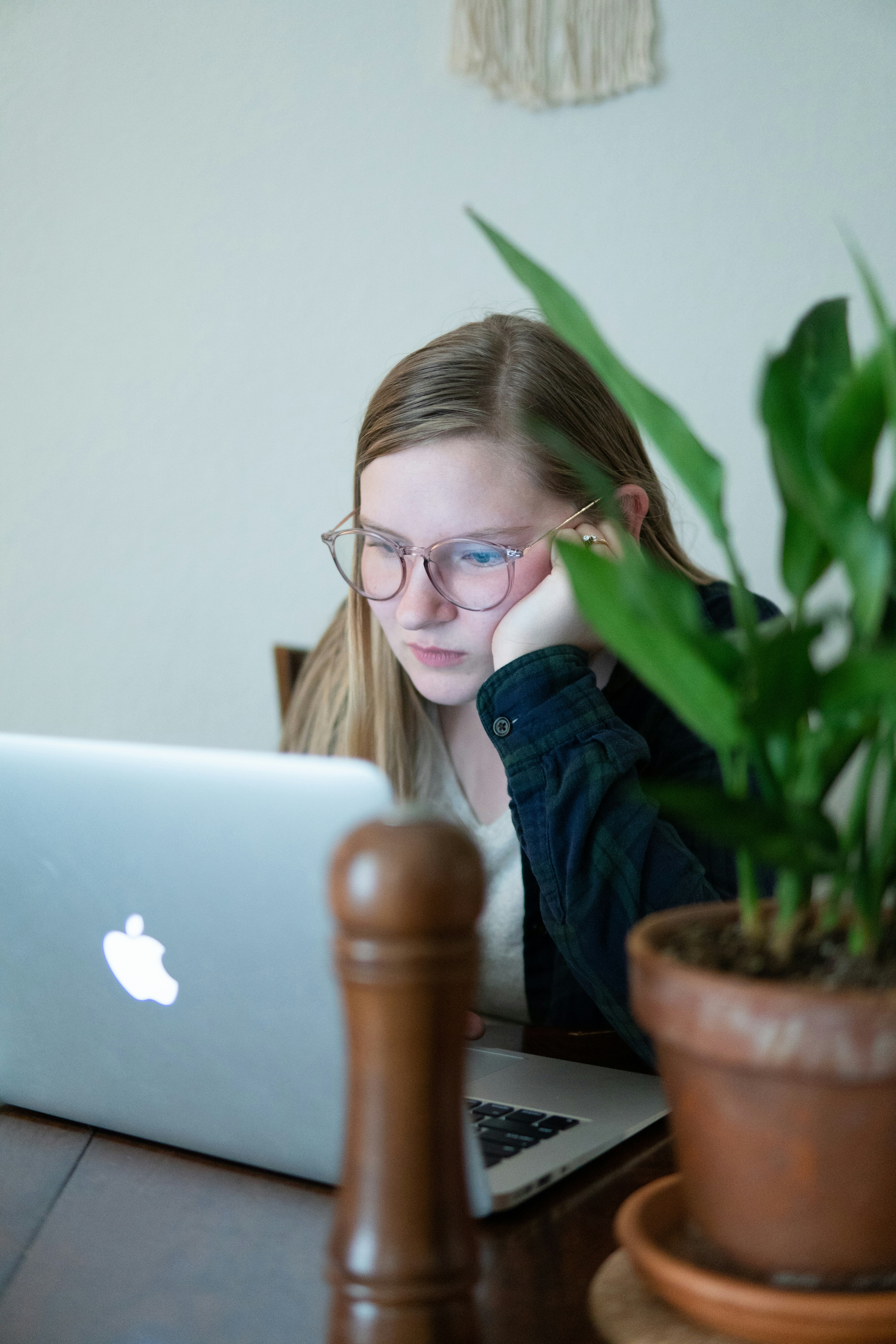 woman in blue denim jacket wearing eyeglasses sitting beside table with macbook