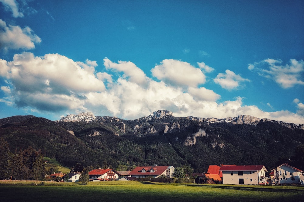 red and white house near green grass field and mountain under blue sky and white clouds