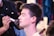 A person is having makeup applied by a makeup artist, with their eyes closed and a brush near their cheek. The focus is on the serene expression of the person receiving the makeup, while the artist is partly in view, concentrating on the task.