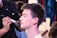 A person is having makeup applied by a makeup artist, with their eyes closed and a brush near their cheek. The focus is on the serene expression of the person receiving the makeup, while the artist is partly in view, concentrating on the task.