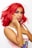 A person with bright red hair styled in waves, wearing bold pink makeup with sparkly accents on the eyelids. They have long yellow nails and are dressed in a sleeveless top featuring a colorful design. The background is plain white, highlighting the vivid colors of the hair and makeup.
