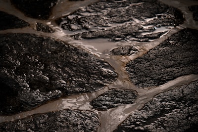 Wet, rough-textured stone surfaces are arranged in an irregular, interlocking pattern. The stones have a dark, almost black appearance with a glossy sheen due to water. The spaces between the stones are filled with lighter colored grout.