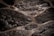 Wet, rough-textured stone surfaces are arranged in an irregular, interlocking pattern. The stones have a dark, almost black appearance with a glossy sheen due to water. The spaces between the stones are filled with lighter colored grout.