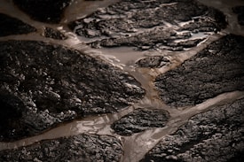 Wet, rough-textured stone surfaces are arranged in an irregular, interlocking pattern. The stones have a dark, almost black appearance with a glossy sheen due to water. The spaces between the stones are filled with lighter colored grout.