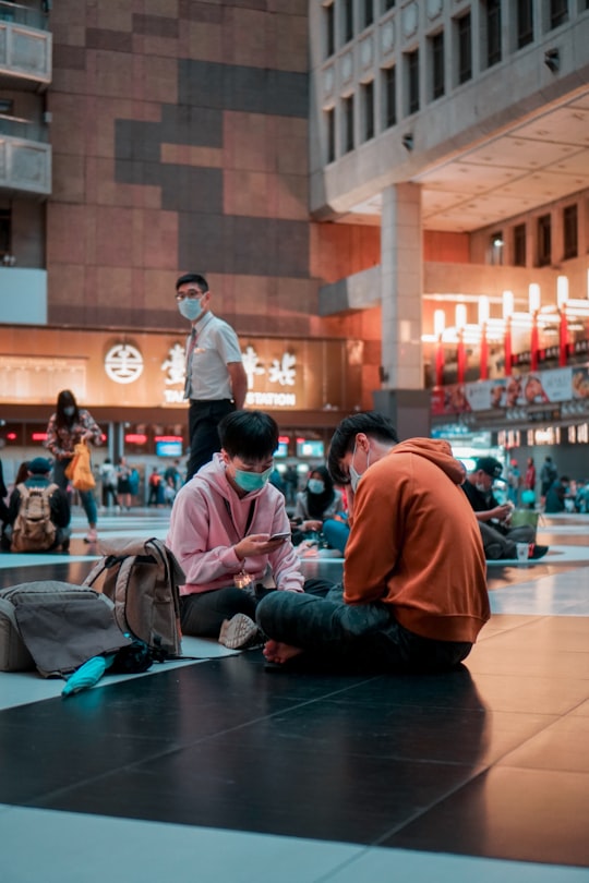 man in red long sleeve shirt sitting on floor in Taipei Main Station Taiwan