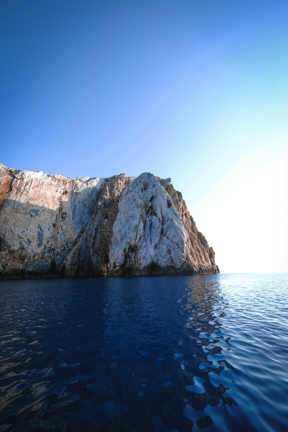 brown rocky mountain beside blue sea under blue sky during daytime