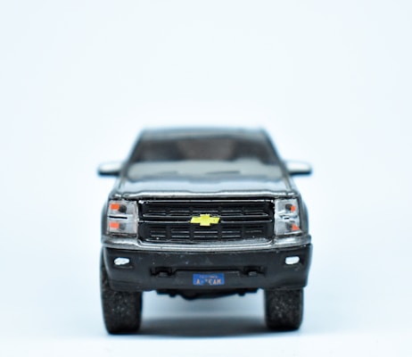 A miniature model of a black Chevrolet truck is displayed with a focus on the front grille and the distinctive yellow Chevrolet logo. The details include the headlights and a small license plate with indistinct text.