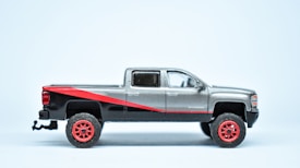 A detailed model of a pickup truck with a silver and black body, accented by a diagonal red stripe. The wheels are red, and the truck is viewed from the side against a plain light background.