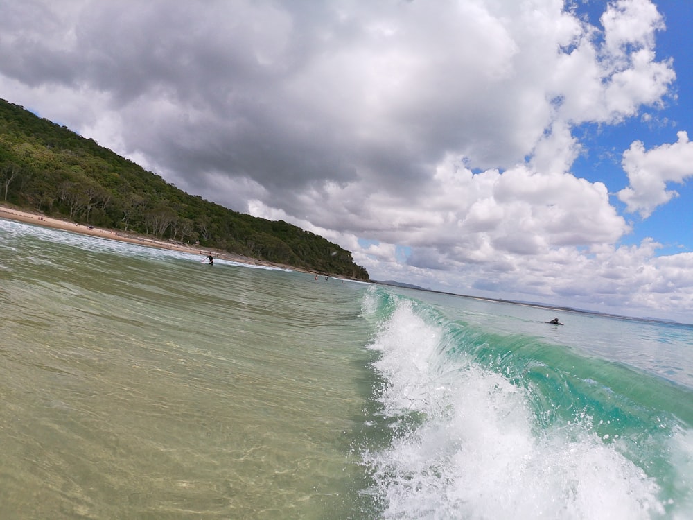 people surfing on sea waves under white clouds and blue sky during daytime