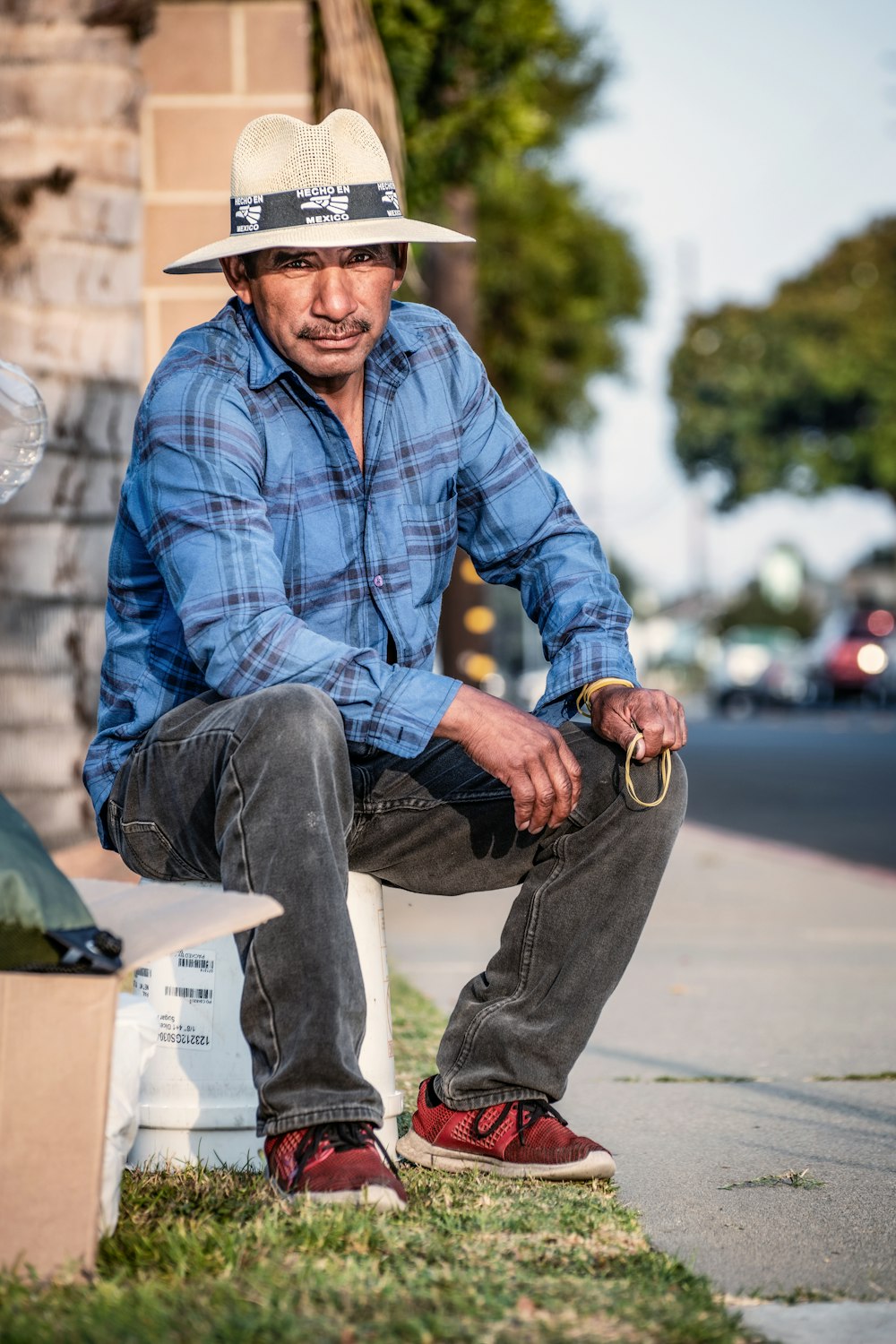 Hombre con camisa de vestir a cuadros azul y blanco y jeans de mezclilla grises sentado en un banco verde