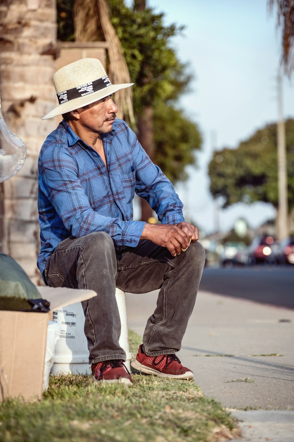 man in blue and white plaid dress shirt and blue denim jeans sitting on gray concrete