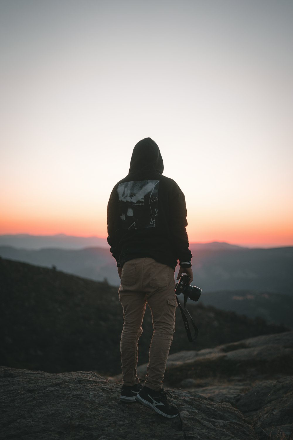 man in black and white hoodie and brown pants standing on rock during sunset