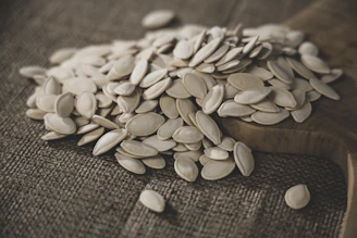 Close-up of glossy pumpkin seeds spilling from a rustic wooden bowl.