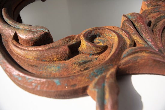 An ornate wooden surface with intricate carvings features a rust-like patina, giving it an aged appearance. Flecks of blue are visible, adding an unexpected touch of color amidst the generally warm tones.