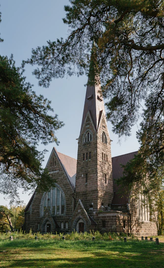 Sunlight filters through trees around the church building with welcoming doors open wide.