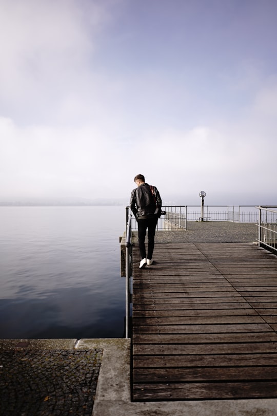 man in black jacket and black pants standing on dock during daytime in Lindau Germany