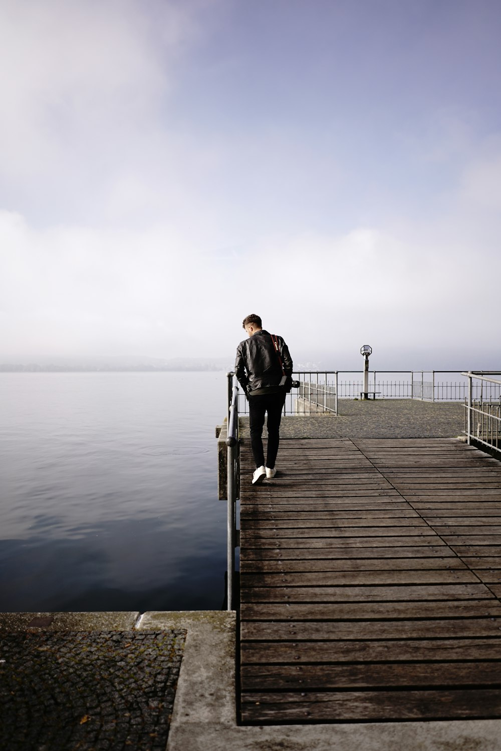 man in black jacket and black pants standing on dock during daytime