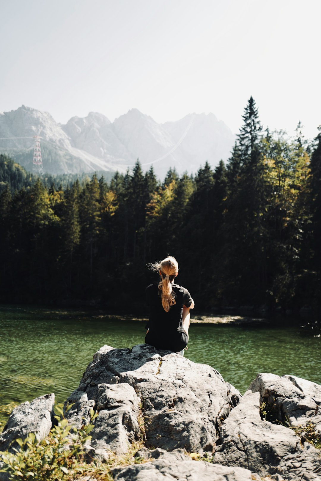 woman in black shirt sitting on rock near green trees during daytime