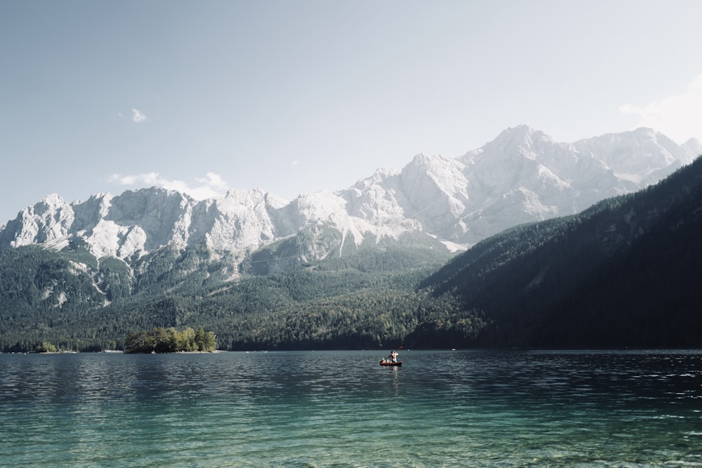 person in red shirt riding on boat on lake near mountain during daytime