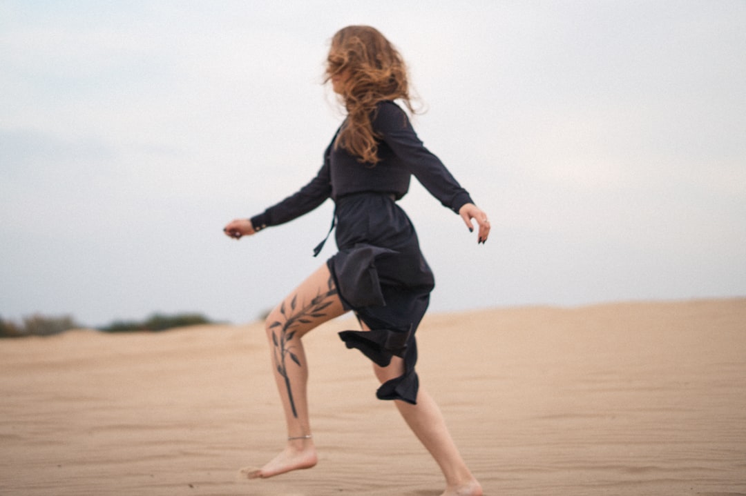 woman in black long sleeve shirt running on brown sand during daytime