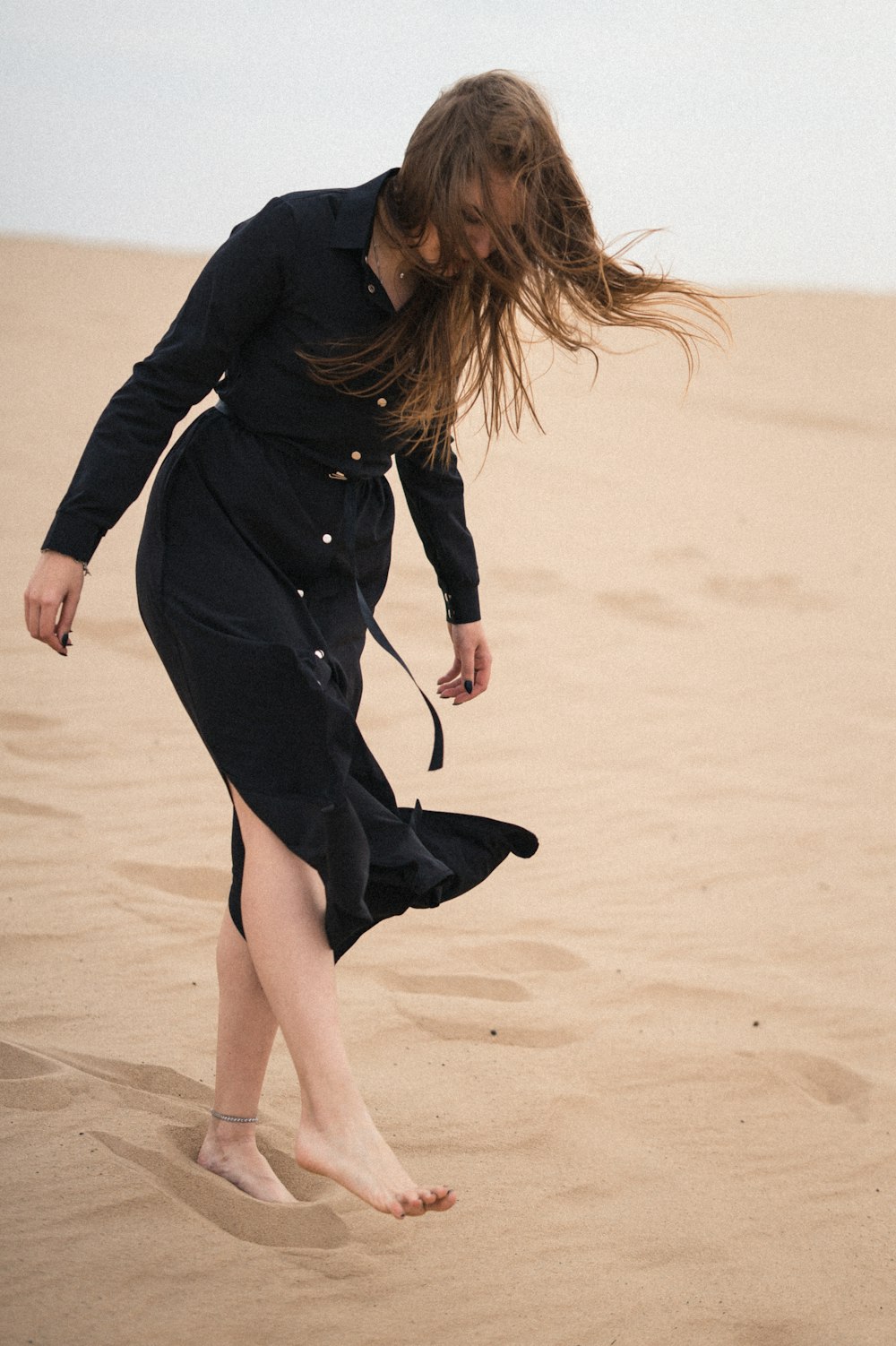 woman in black long sleeve dress walking on sand during daytime