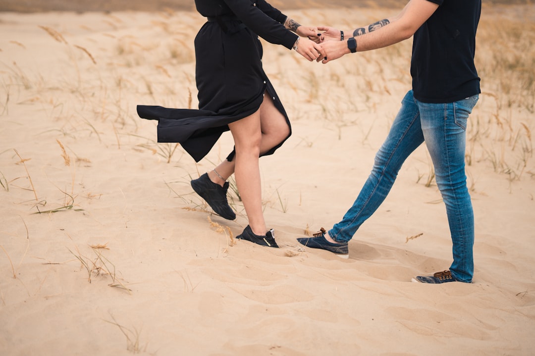 woman in black shirt and blue denim jeans walking on white sand during daytime