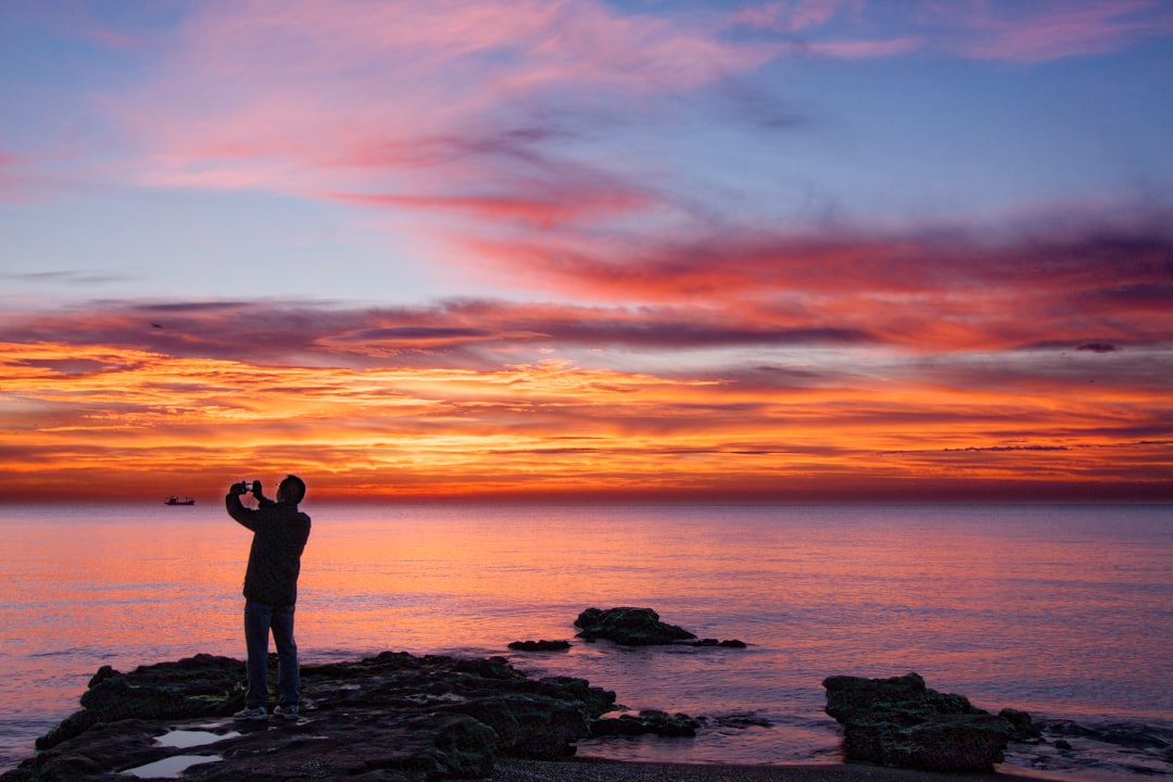 silhouette of woman standing on rock formation near body of water during sunset