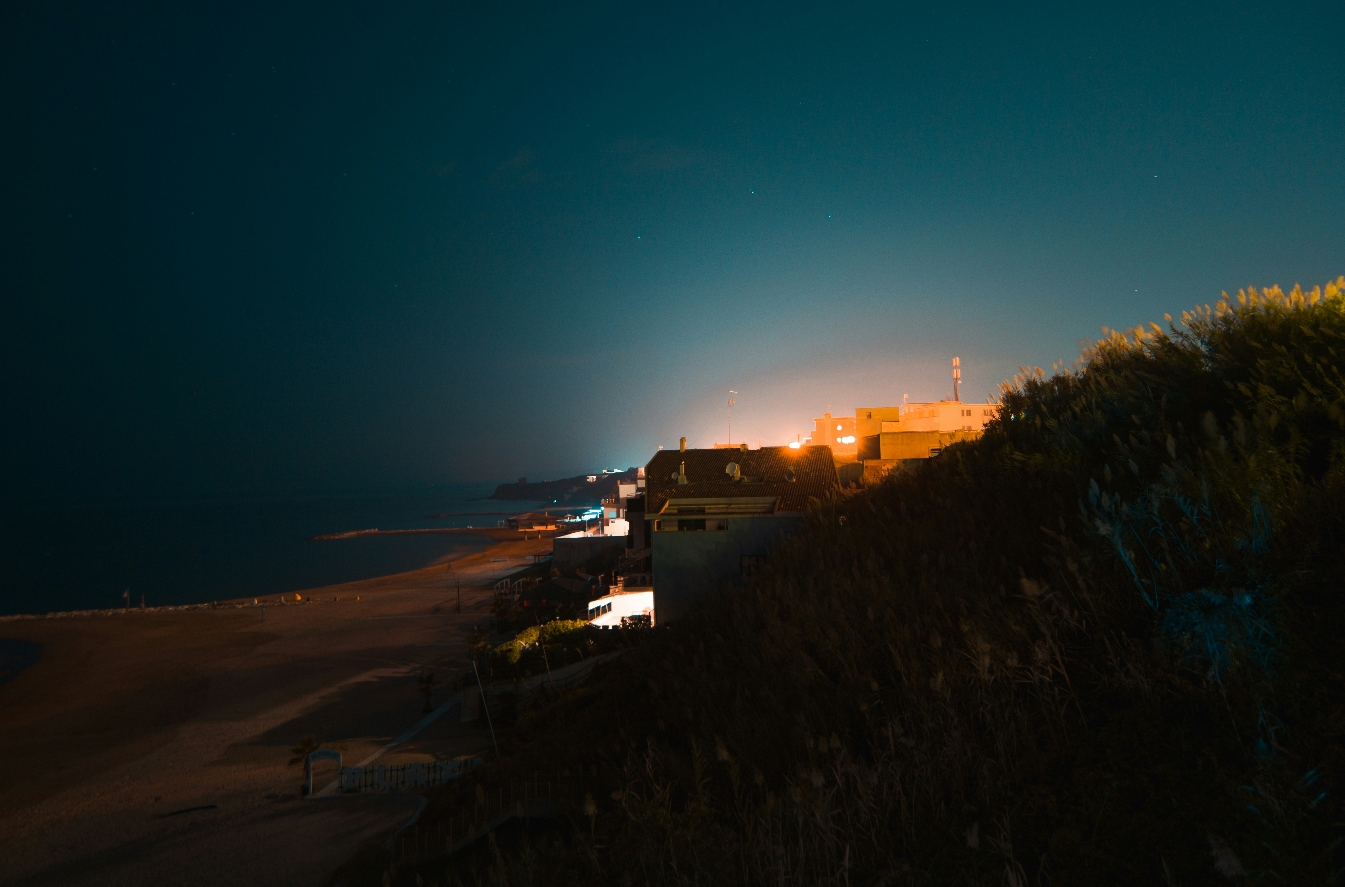 A chaotic scene on a beach at night, with people running, blurry figures, and a sense of tension. Bright lights from nearby shacks illuminate parts of the scene.