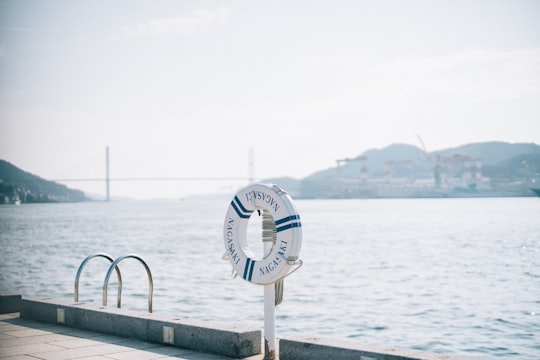 white and blue round analog watch on gray metal railings near body of water during daytime in Nagasaki Japan