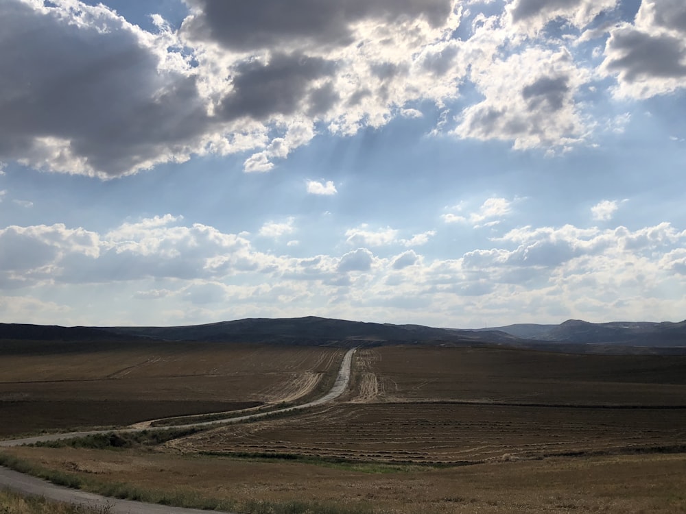 brown field under blue sky and white clouds during daytime