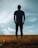A person stands in a field of tall grass under a vast sky. The individual is facing away, gazing into the open space, creating a sense of contemplation and solitude.