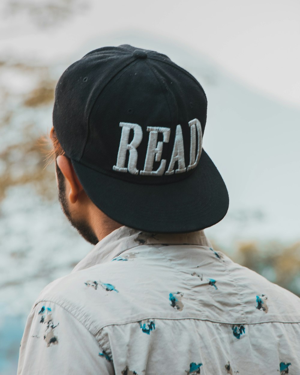 man in white and blue bird print shirt wearing black cap