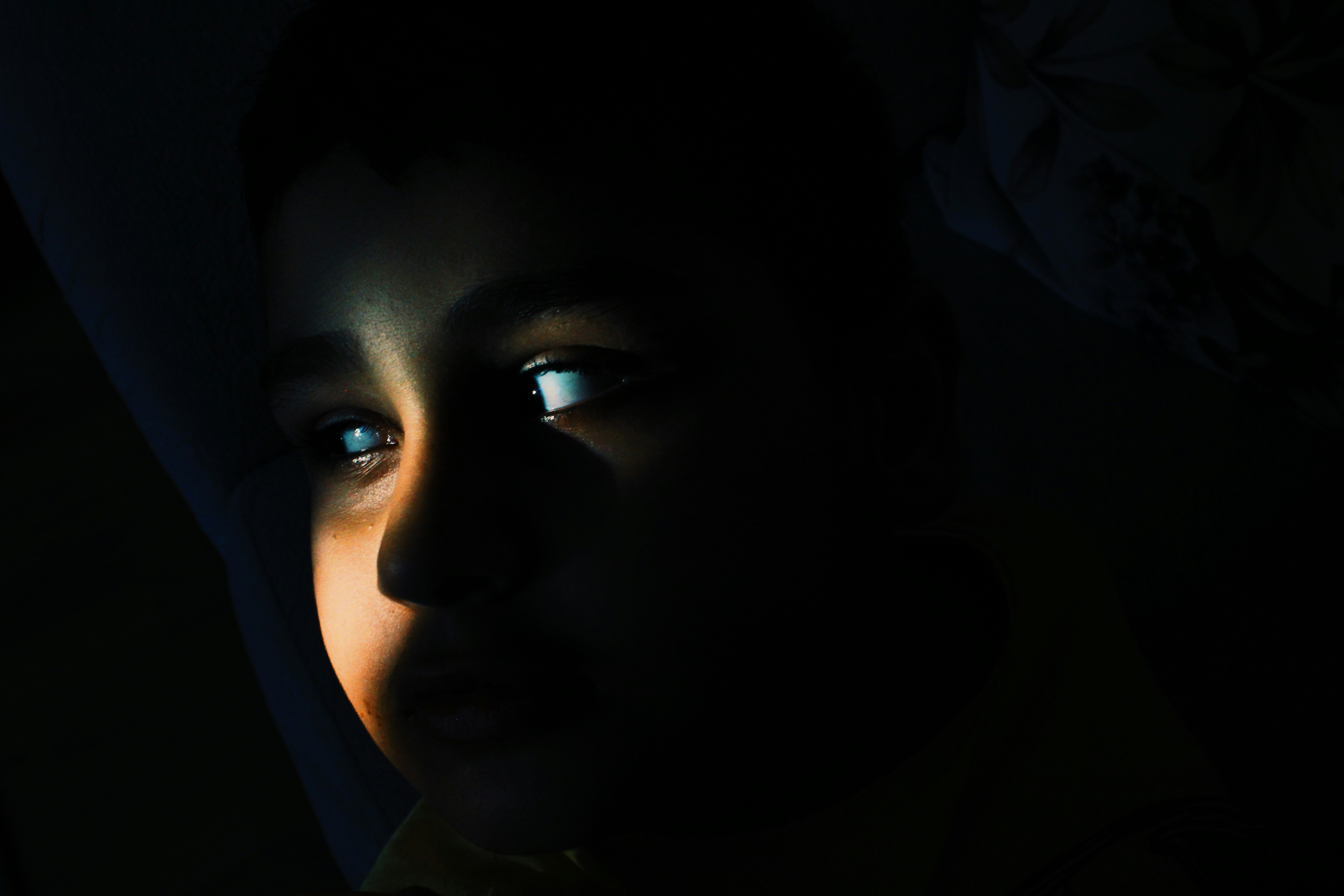 A child looking engrossed in a phone, screen light reflecting on face, in a slightly dark room, perhaps late at night.