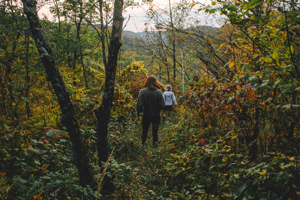 man in black jacket and black pants standing in front of green and brown trees during