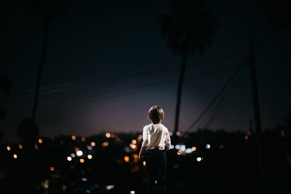 child in white t-shirt and blue denim jeans standing on the ground during night