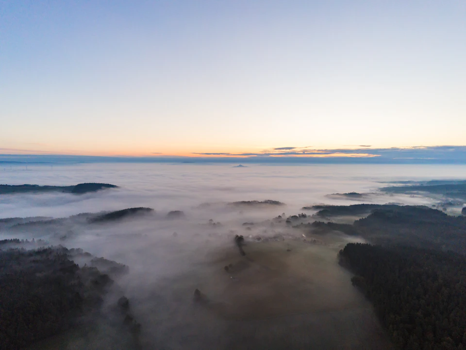 Fog-covered fields stretch out into the distance under a thick, hazy blue sky